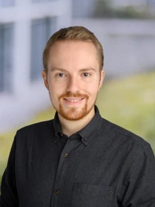 Profilfoto von Paul. Er hat kurzes blondes Haar, braune Augen, einen gepflegten Bart und lächelt in einem dunkelgrauen Hemd vor unscharfem Hintergrund.